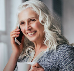 Lady smiling on the phone whilst drinking a coffee